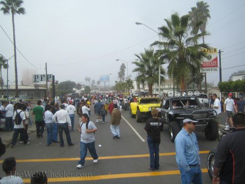 1990 Ford Bronco - foggy crowded street packed with spectators and off-road race vehicles, with palm trees and Tecate beer signage.
