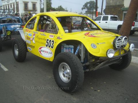 1990 Ford Bronco - yellow VW Beetle-bodied Baja race car numbered 503 with twin Hella lights and sponsor decals on a street.