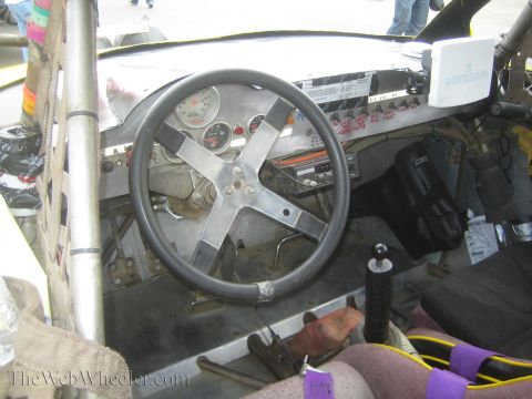 1990 Ford Bronco - Interior of an off-road race car showing a polished aluminum steering wheel, gauge cluster, shifter and Lowrance unit.