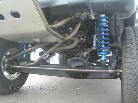 1990 Ford Bronco - Close underside view of an off-road vehicle's rear suspension with blue coilover shocks and tubular control arms.