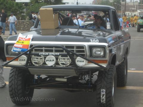 1990 Ford Bronco - Front view of a black Ford pickup race truck numbered 300 with a row of Hella and PIAA lights and a Stupid Hurts banner.