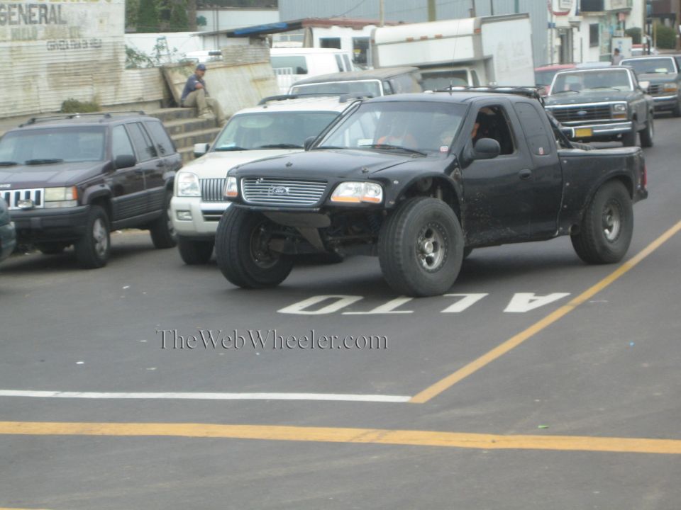 Black Ford pickup with off-road suspension driving on a city street