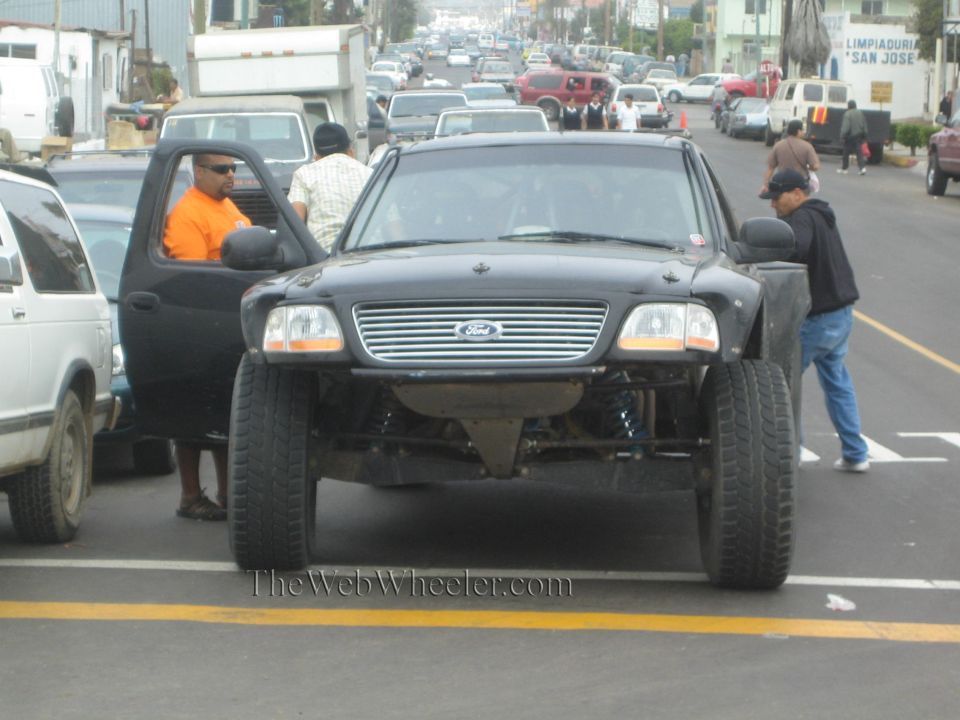 Black Ford pickup with exposed prerunner suspension on a street