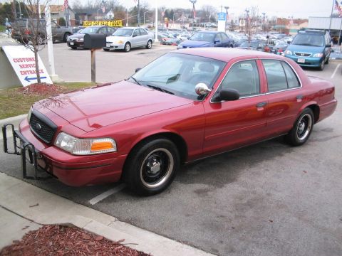 2001 Ford Crown Victoria - A red sedan, possibly a 2001 Ford Crown Victoria, is parked in a lot with a push bumper attached.