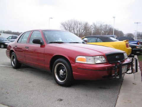 2001 Ford Crown Victoria - A red 2001 Ford Crown Victoria sedan is parked in a lot, with other vehicles visible in the background.