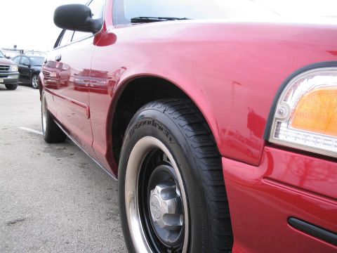 2001 Ford Crown Victoria - A red 2001 Ford Crown Victoria is shown from a low angle, highlighting its front fender and wheel area.