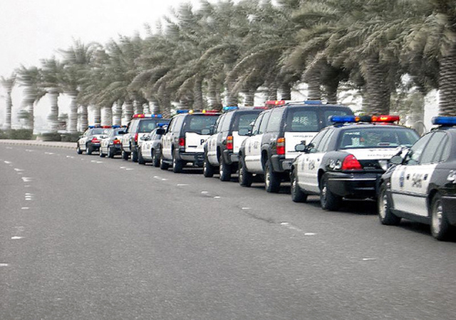 Line of black-and-white police sedans and SUVs parked along a palm-lined roadside