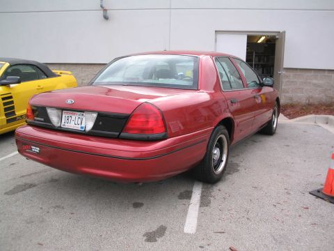 2001 Ford Crown Victoria - A red 2001 Ford Crown Victoria is parked next to a yellow Mustang convertible.