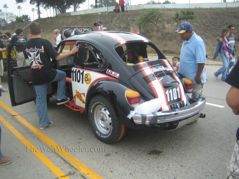 1990 Ford Bronco - Black Baja-style VW Beetle race car numbered 1101 with red striping and roll cage, surrounded by spectators at a roadside event.