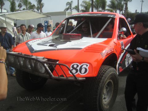 1990 Ford Bronco - orange and white number 86 off-road race truck is examined by officials as spectators crowd around at an event.