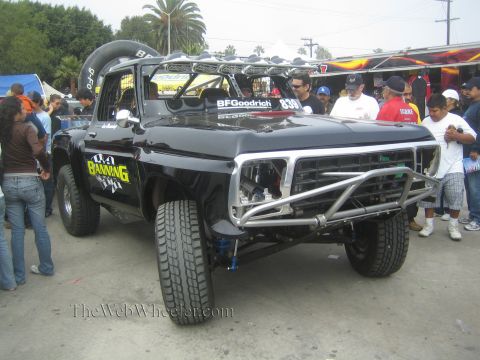 1990 Ford Bronco - black classic Ford pickup prerunner with chrome tube bumper and 'Banning' graphics draws a crowd at an outdoor event.