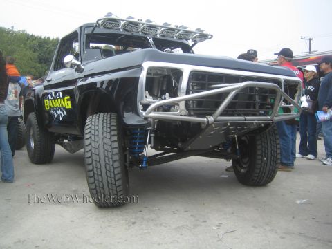 1990 Ford Bronco - Low front view of a black 'Banning' Ford prerunner showing chrome tube bumper and long-travel blue-coilover suspension.