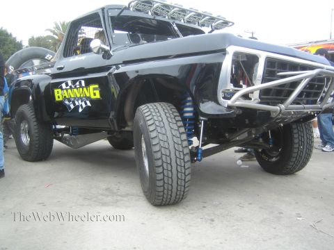 1990 Ford Bronco - Side-front view of a black classic Ford 'Banning' prerunner with blue coilovers and exposed long-travel suspension.