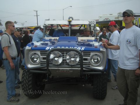1990 Ford Bronco - blue and silver early Ford Bronco off-road truck number 302 with multiple lights is surrounded by spectators.