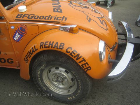1990 Ford Bronco - Close-up of an orange Beetle race car's front fender showing steel wheel, mud tire and Spinal Rehab Center lettering.