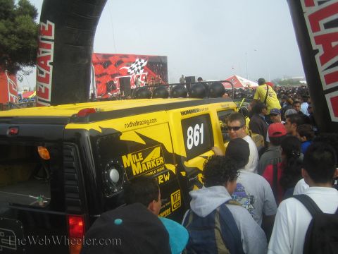 1990 Ford Bronco - yellow-and-black Hummer race truck numbered 861 with Mile Marker and roof lights surrounded by a dense crowd near a start arch.