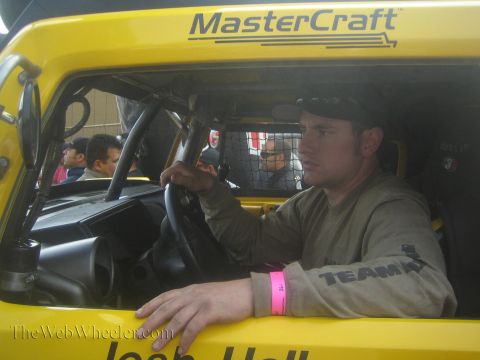 1990 Ford Bronco - man wearing a cap and pink wristband grips the wheel inside a yellow caged race vehicle marked MasterCraft.