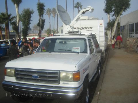 1990 Ford Bronco - white Ford Bronco mounted with a Trail-Gator satellite uplink dish sits at a broadcast staging area lined with palm trees.