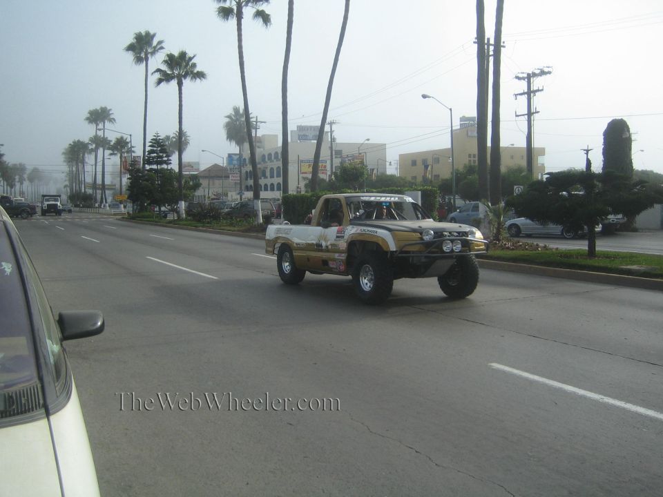 White and gold off-road prerunner truck driving down a palm-lined boulevard