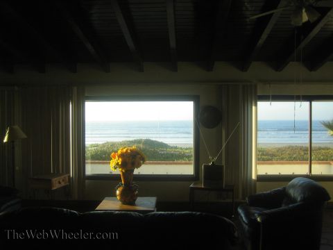 1990 Ford Bronco - dim living room with a flower vase on a table looks out through large windows onto a beach and ocean.