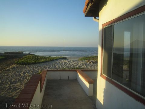 1990 Ford Bronco - walled patio of a beach house overlooks dunes, a sandy beach and the ocean under a clear sky.