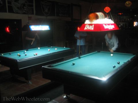 1990 Ford Bronco - Two people shoot pool on green-felt tables lit by Bud and Coors beer lamps inside a dim bar.