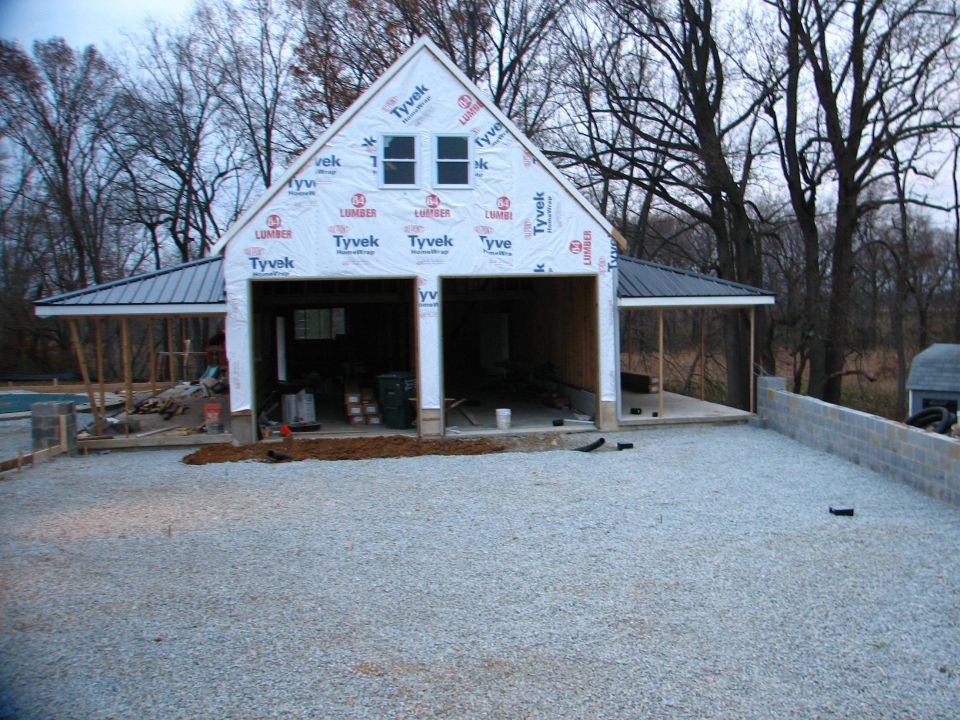 Two-bay garage under construction wrapped in Tyvek with gravel apron