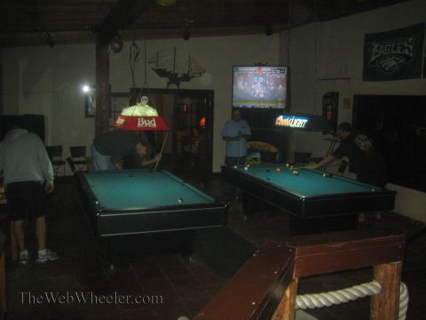 1990 Ford Bronco - Several people play at two lit pool tables in a dim sports bar with Eagles banners and a wall-mounted TV.