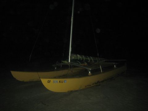 1990 Ford Bronco - small yellow-hulled catamaran sailboat sits beached on dark sand at night, showing CF registration numbers.