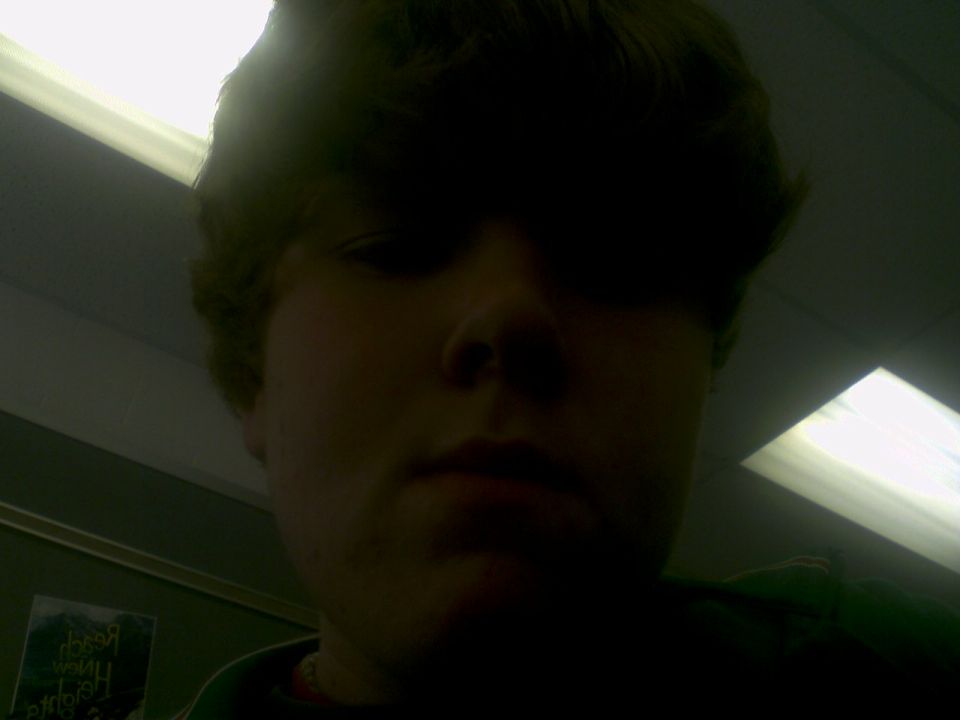 Person's face in shadow, with overhead lights and a poster on the wall