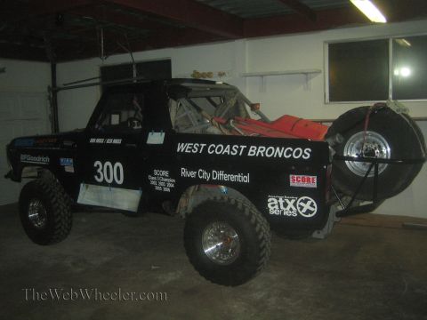 1990 Ford Bronco - black West Coast Broncos number 300 off-road race truck is parked in a garage under fluorescent light.