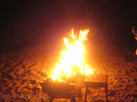 1990 Ford Bronco - tall bonfire blazes bright orange on a sandy beach at night with chairs placed in front of it.