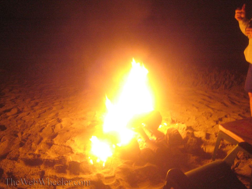 Bonfire burning on a beach at night with a person standing at right