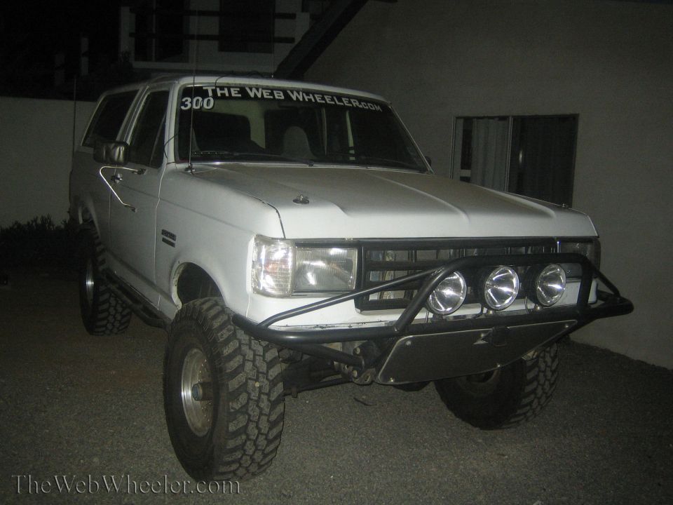 White lifted Ford Bronco with light bar and grille lights at night