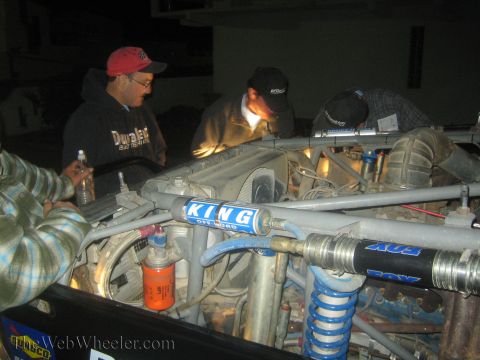1990 Ford Bronco - Men in caps work on a tube-chassis off-road truck at night, with King and Fox coilover shocks prominent in the foreground.