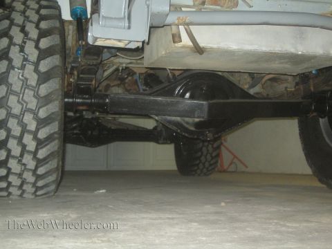 1990 Ford Bronco - underbody view shows a truck's rear solid axle, control arm, leaf spring and large off-road tires over a garage floor.