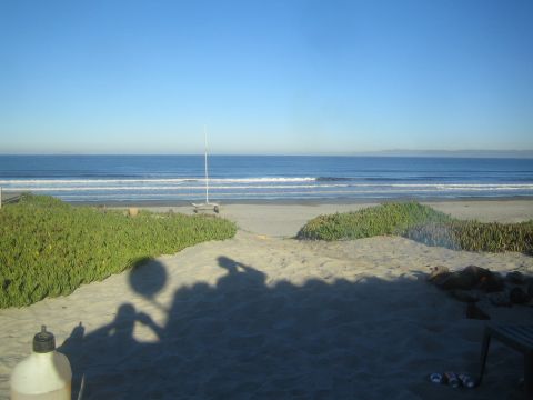 1990 Ford Bronco - sandy beach foreground with iceplant dunes leads to a volleyball net and gentle ocean surf under a clear blue sky.
