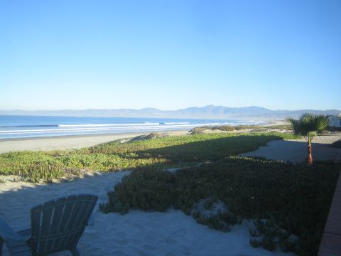 1990 Ford Bronco - From a patio with a wooden chair, green dune plants and a palm frame a view of ocean surf and distant coastal mountains.