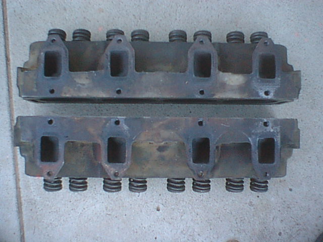 Two engine cylinder heads showing intake port faces on concrete