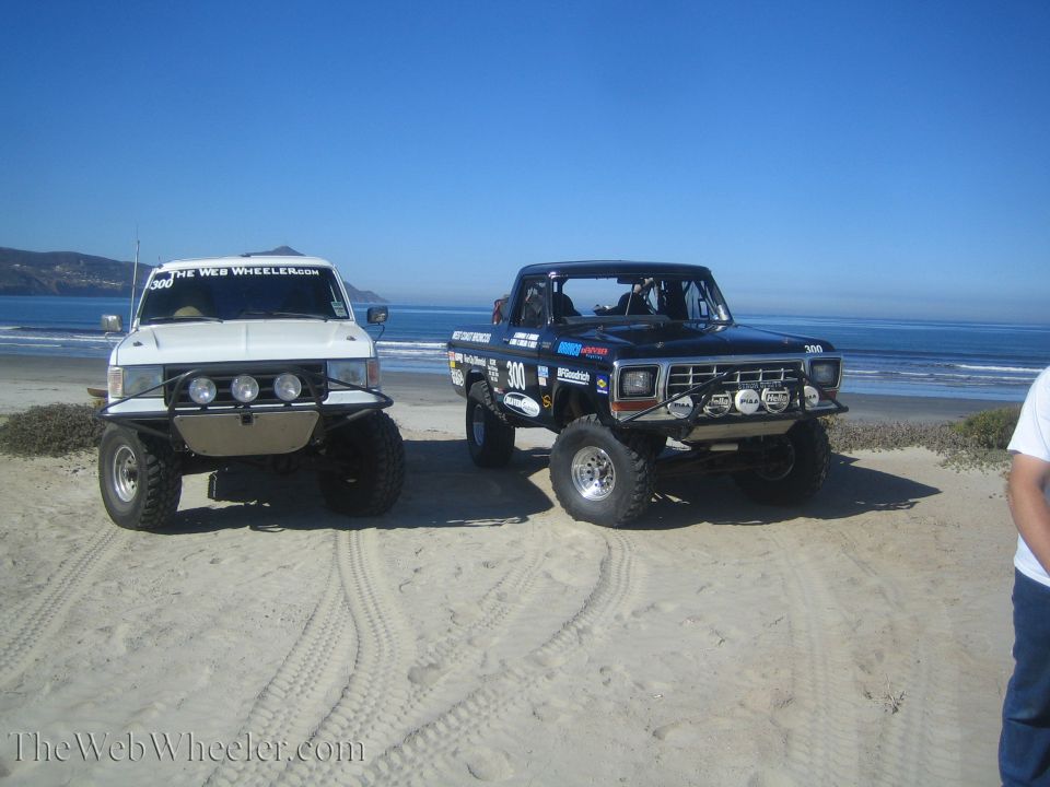 White lifted SUV and black number 300 race truck parked side by side on a beach