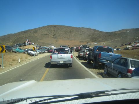1990 Ford Bronco - View through a windshield of pickups on a desert highway approaching a hill crowded with parked vehicles and spectators.