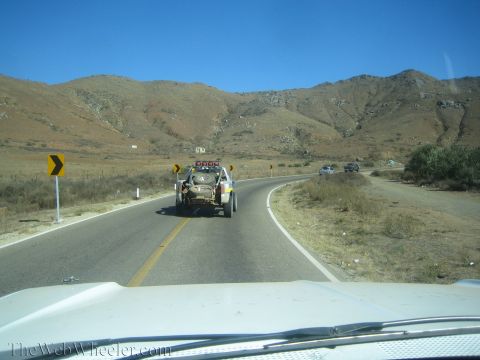 1990 Ford Bronco - View through a windshield of an off-road vehicle being towed along a paved highway winding through arid brown hills.