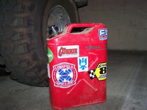 1995 Ford Bronco - A red jerry can adorned with various stickers sits beside a large off-road tire, suggesting a connection to automotive or off-road activiti…