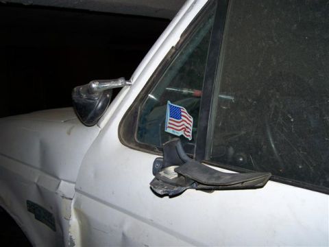 1995 Ford Bronco - Side view of a damaged white truck door and fender with a side mirror and an American flag sticker.