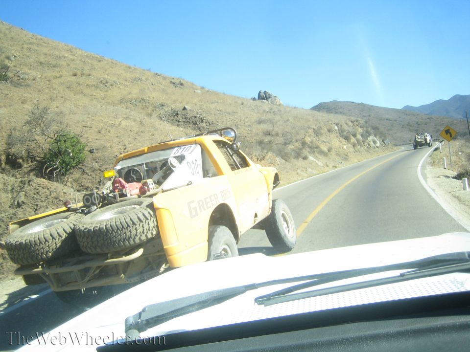 Yellow off-road race truck carrying spare tires on a desert mountain road