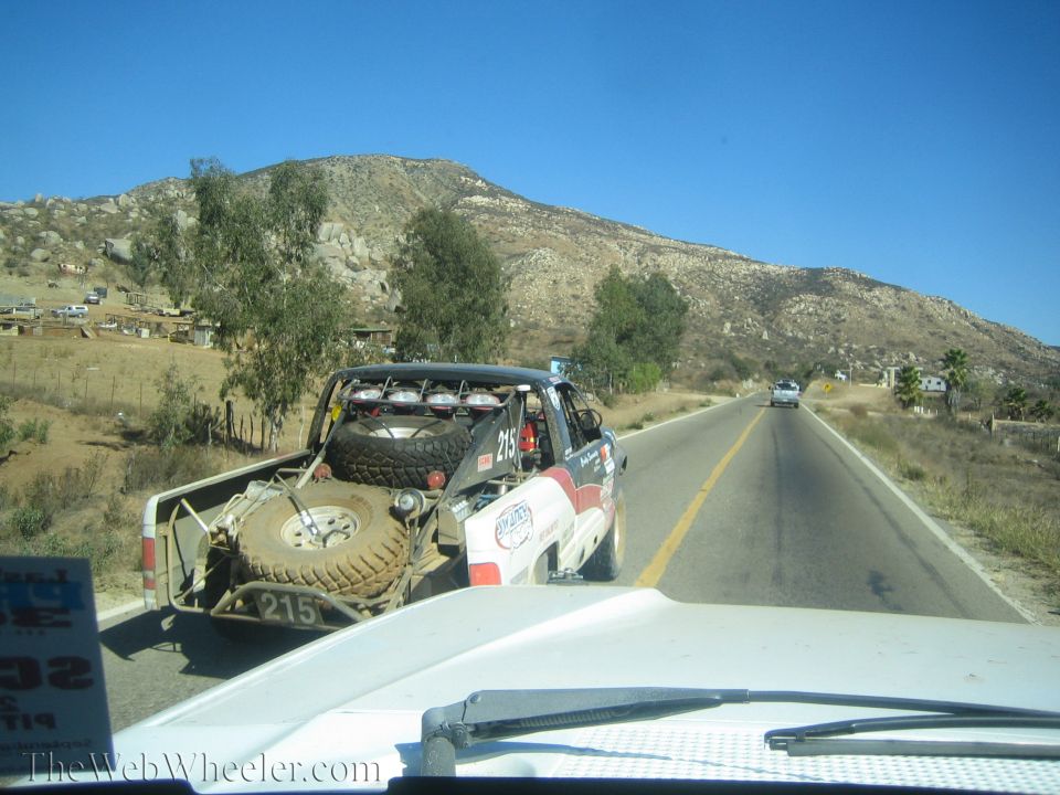 Red and white off-road race truck number 215 on a rural highway