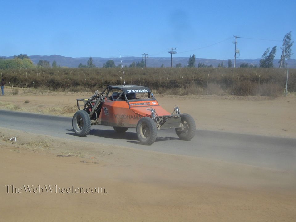 Orange single-seat off-road race buggy on a sandy paved road