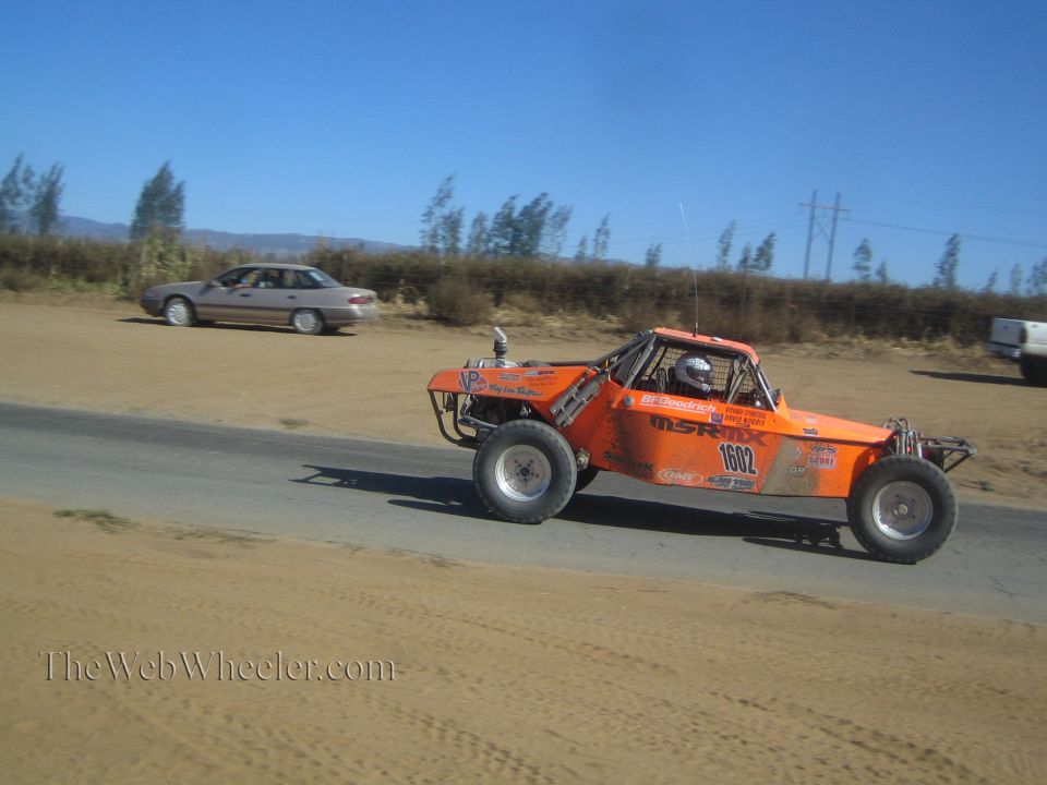 Orange off-road race buggy number 1602 driving past a parked car