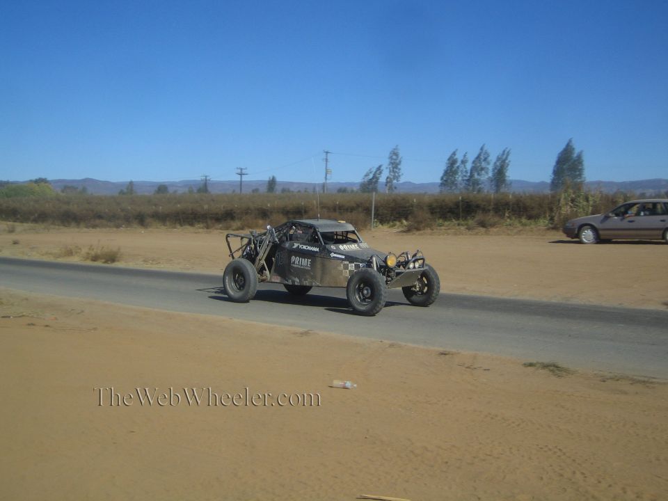 Dark off-road race buggy on a sandy road with a passing car behind