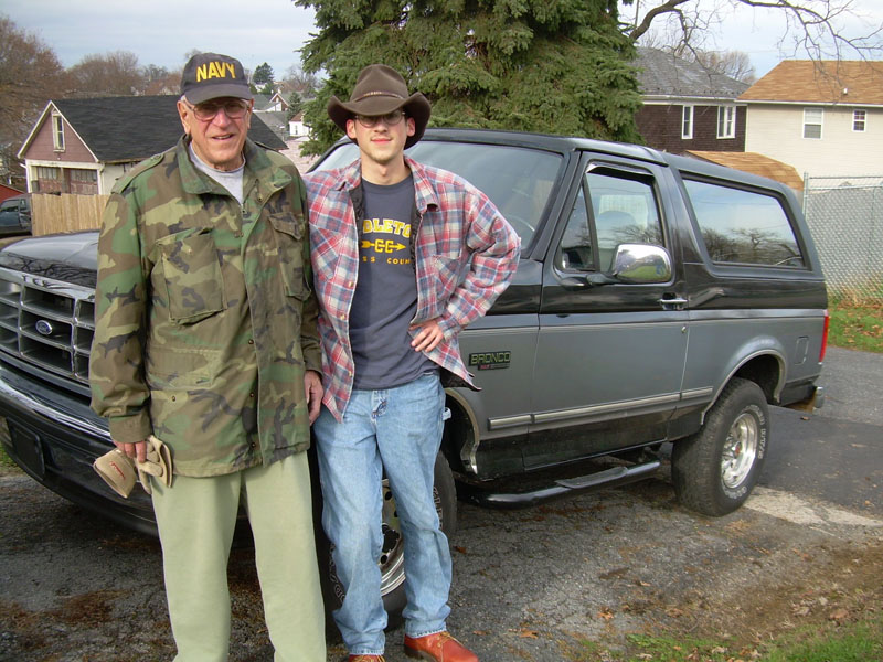 Two men standing in front of a dark Ford Bronco in a driveway